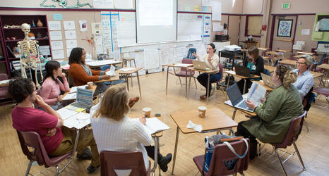 Teachers sitting in a circle in desks discussing a problem