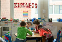 students working together at a table with the word kindness written on the board behind them